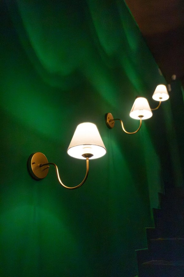 Arandelas de bronze subindo a parede verde ao lado da escada do Coxixo